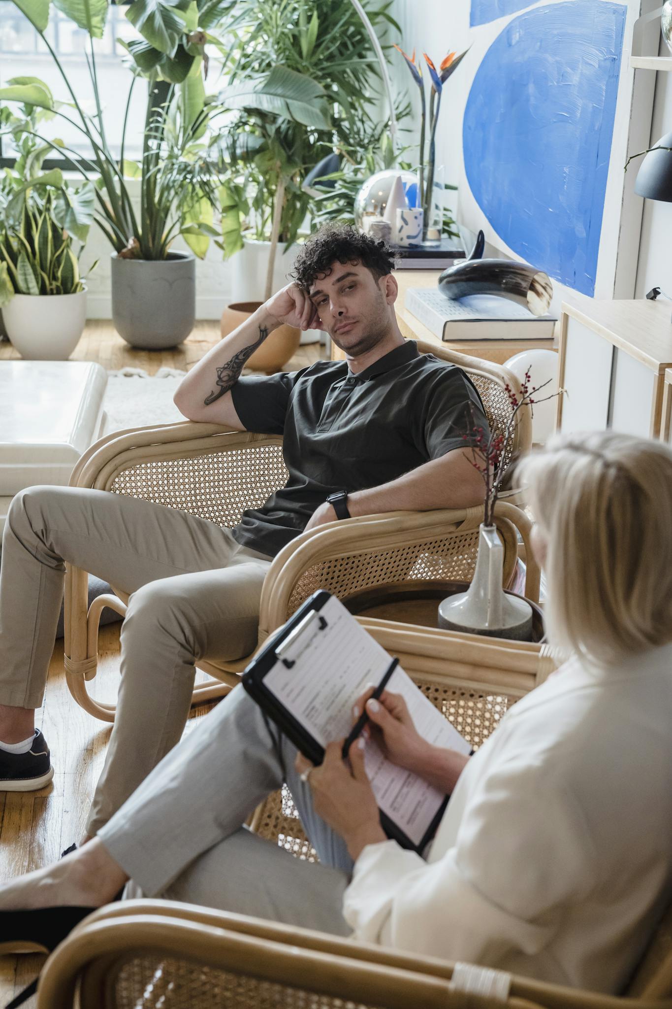 A man and a woman in a therapeutic counseling session in a plant-filled modern office space.